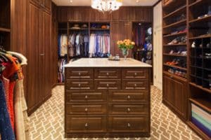 Room-size walk-in closet with marble-topped dark wood chest of drawers in the center, a chandelier above, and matching wood shelves and sliding doors on either side